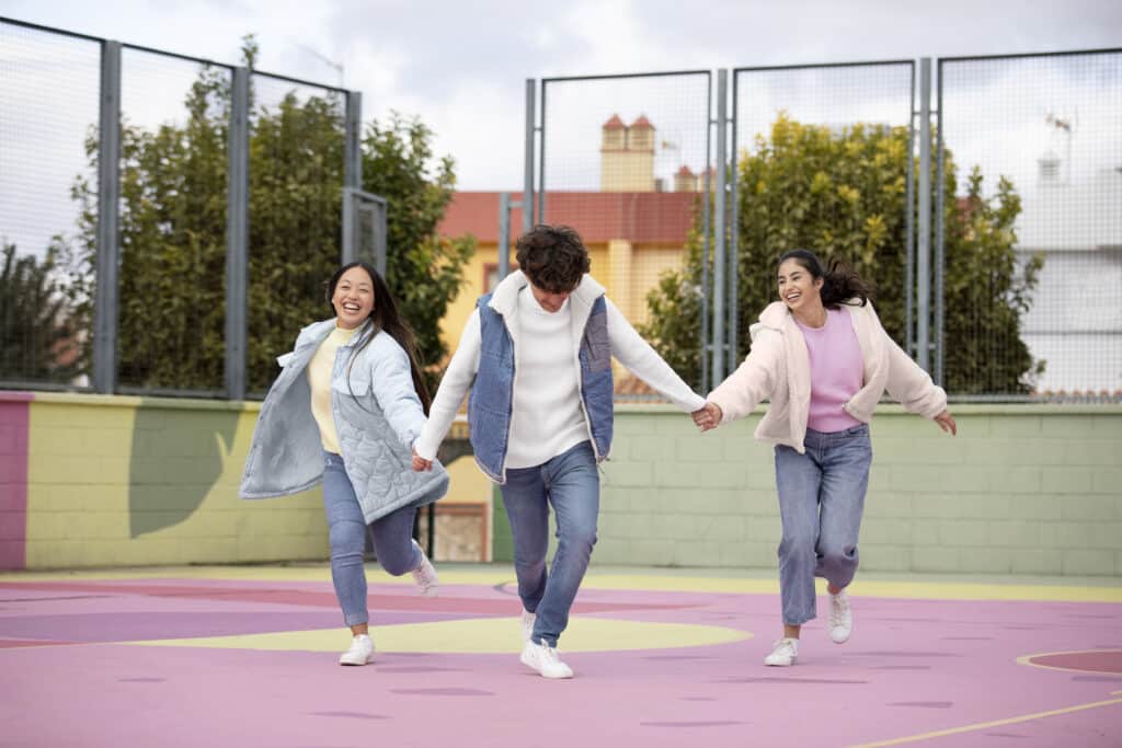 three young students having fun together in a playground. The ground is very colourful and the children look happy.