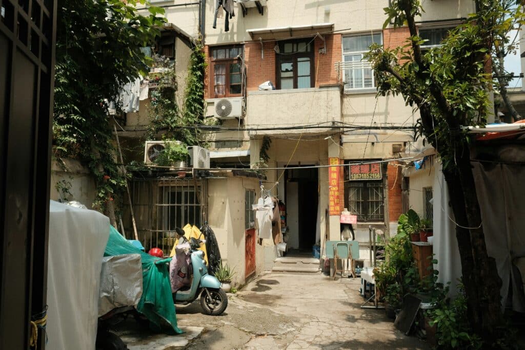 An alleyway in a Chinese town leads to the entrance of a small building. A motorbike is parked in front of the door.