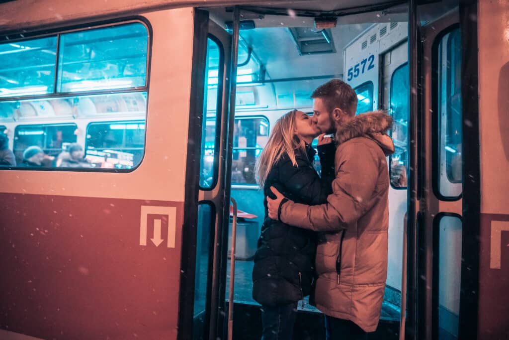 Couple kissing at the door of a moving tram in the middle of a snowy winter.