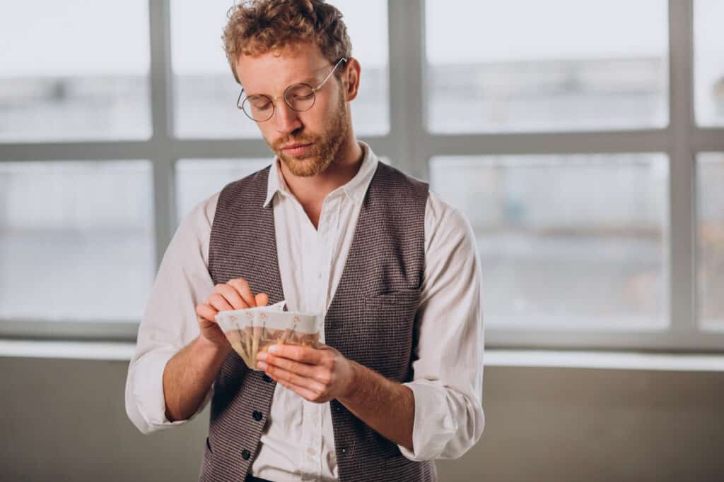 Blond-haired man with glasses counting bills in his hand