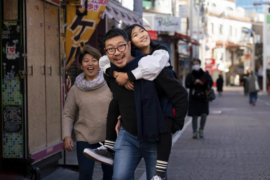 Happy Chinese family, the father carrying his daughter on his back, walking down the street in a Chinese town.