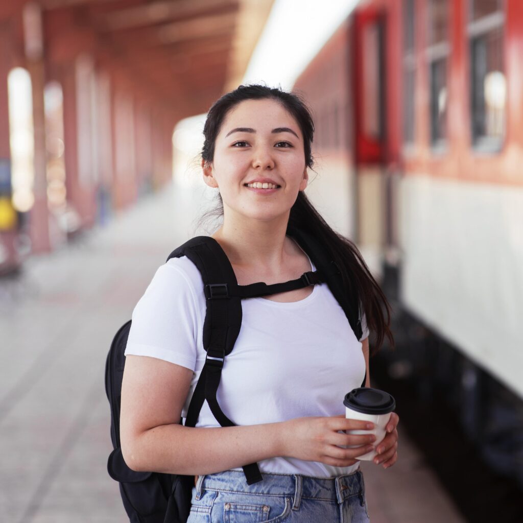 A Chilean student smiling at the camera, she is carrying a rucksack and standing on the platform of a train.