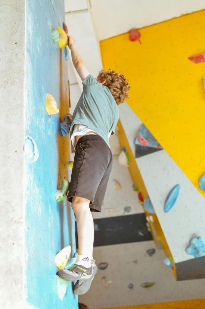 A young boy is climbing on a blue wall, holding on to several holds.