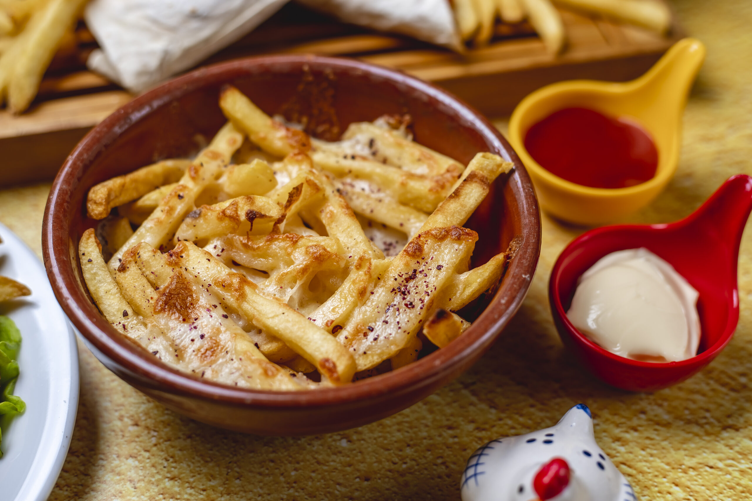 Bowl of chips with melted cheese, ketchup and mayonnaise as side sauces.