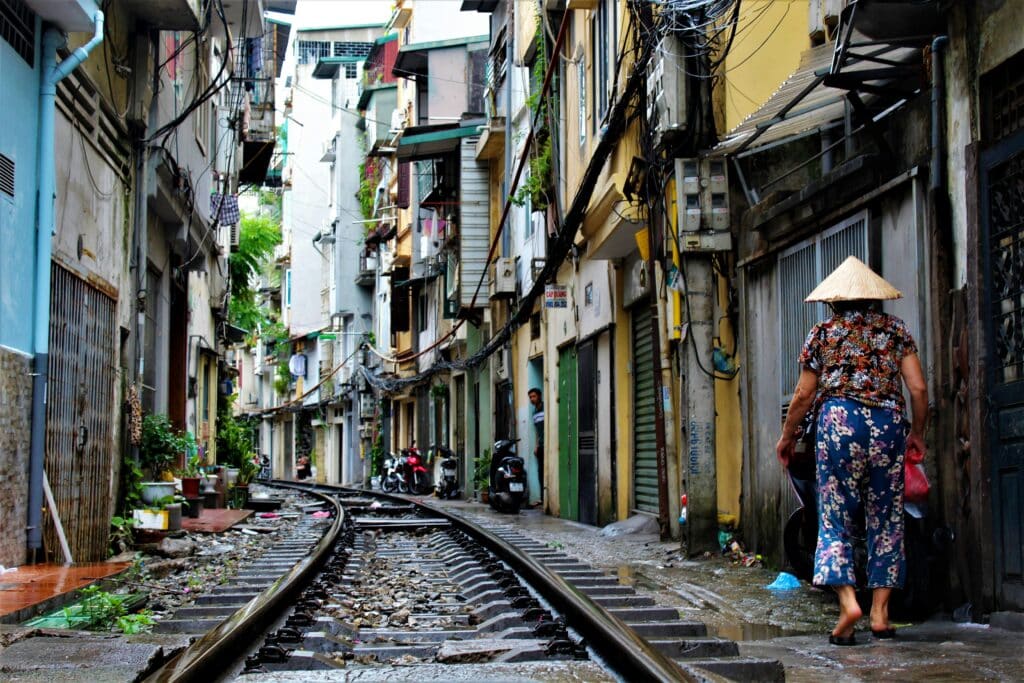 Tight, typical street in Hanoi, Vietnam. A woman wearing a traditional hat walks along the rails that cross the street.