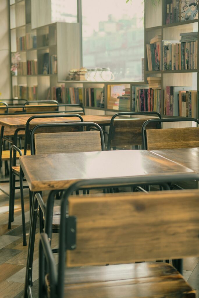 Wooden desks and chairs in a classroom, with a library in the background.