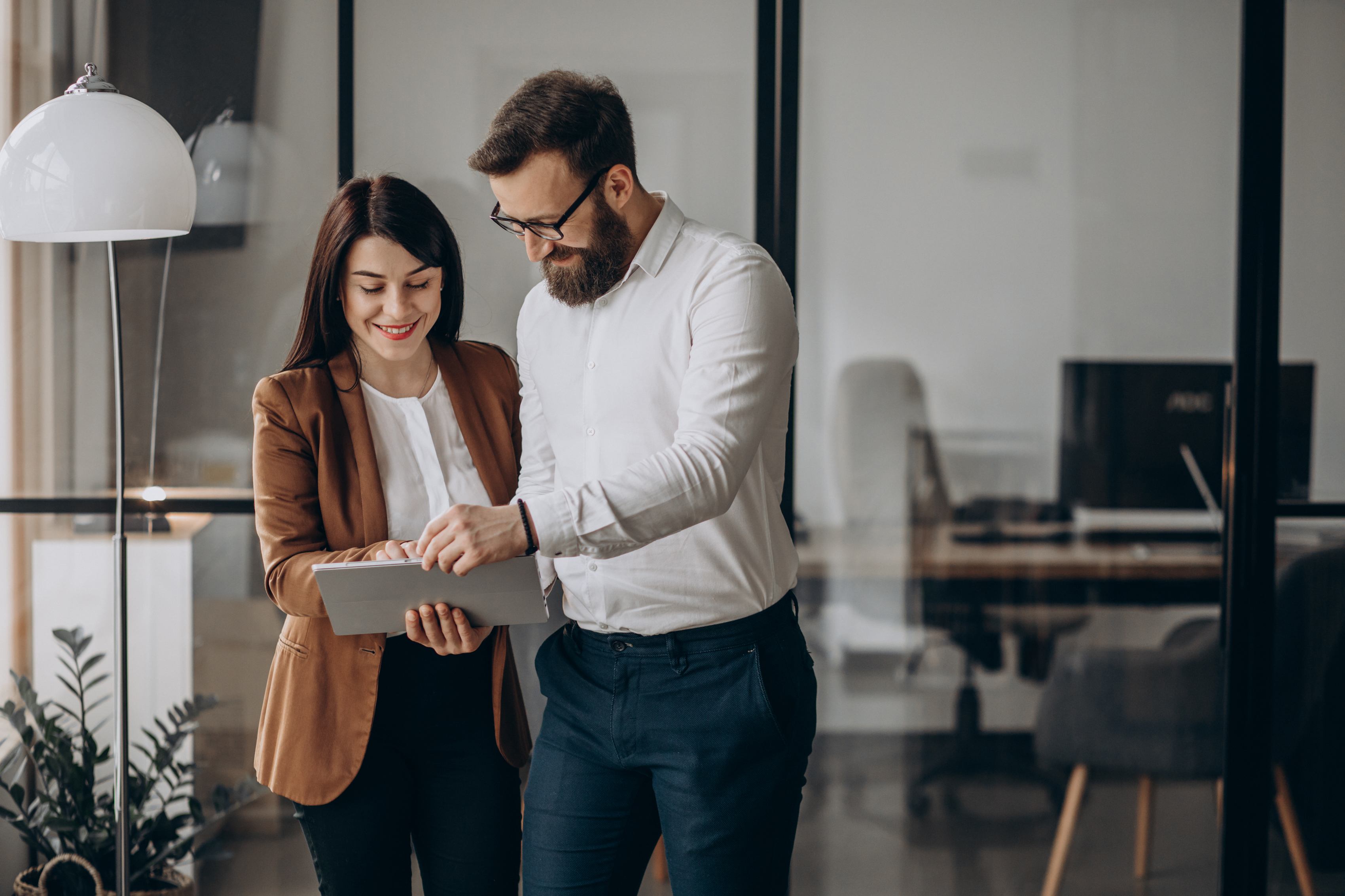 A woman and a man who work together smile as they read on their tablet. They are in a modern office.