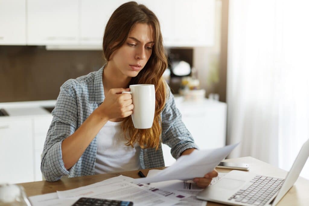 Young woman checking her budget and doing her taxes. She looks worried and doubtful.