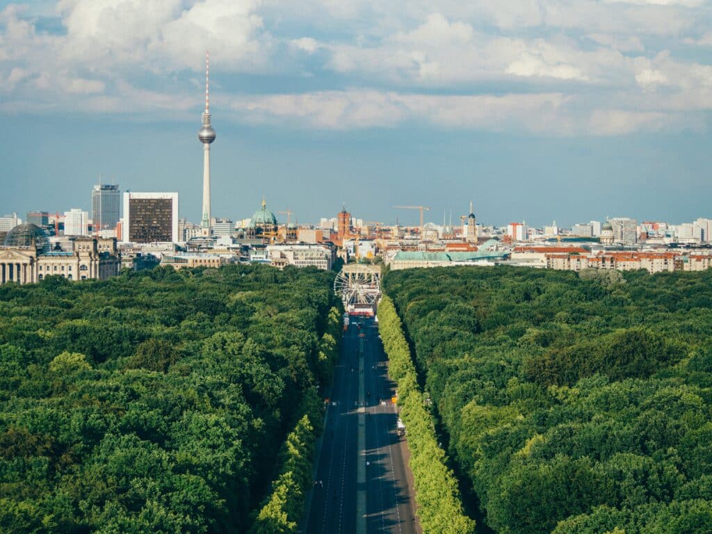 Aerial view of the city of Berlin in Germany, on the main avenue in the middle of a park with a Ferris wheel at the end of the avenue. The television tower dominates the rest of the capital, under a blue sky.