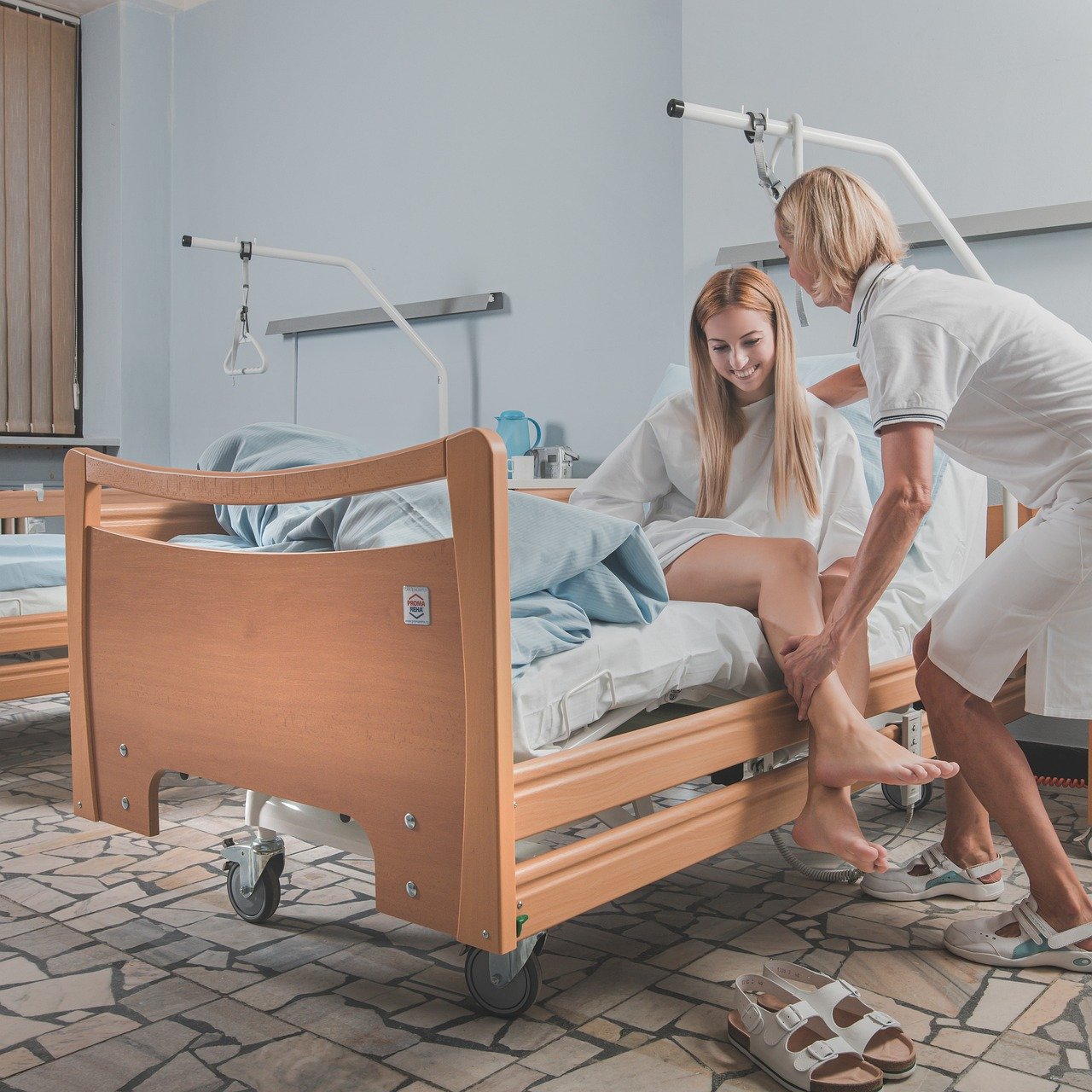 A nurse helps an injured young blonde woman off her hospital bed by supporting her legs.