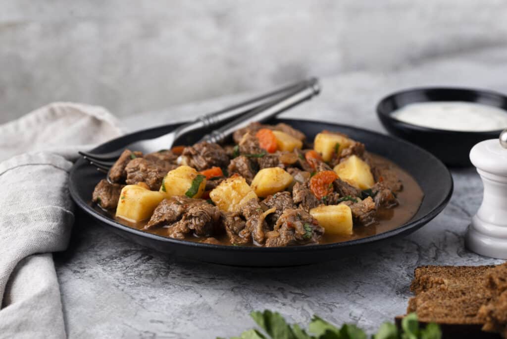 Goulash dish presented in a sleek, modern setting with fork and knife.