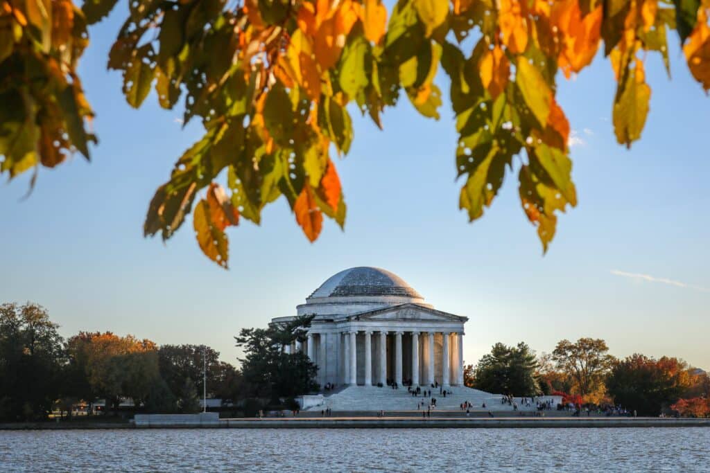 Photograph of the Jefferson Memorial and the Tidal Basin in Washington DC, USA, taken in autumn. Orange tree leaves can be seen at the top of the photograph.