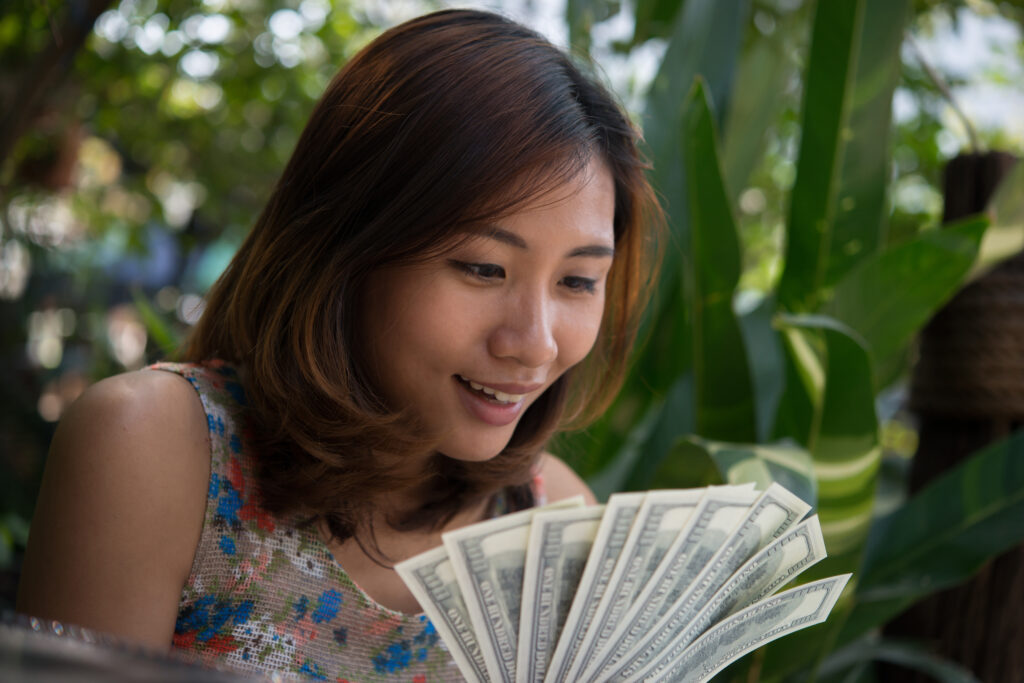 Short-haired Thai woman smiling as she counts a wad of cash in her hand.