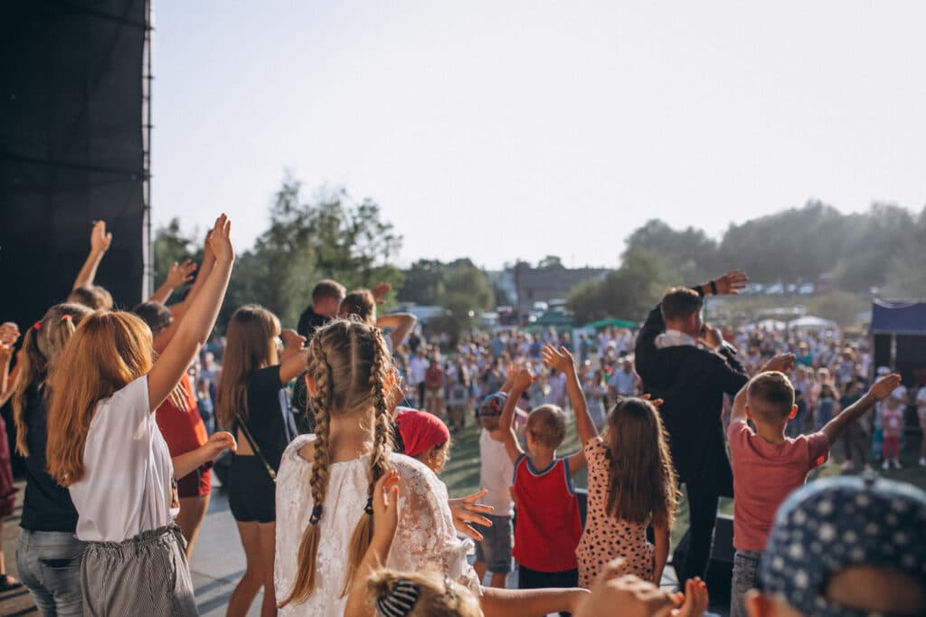 A group of people and children on stage enjoying themselves at an outdoor music festival.