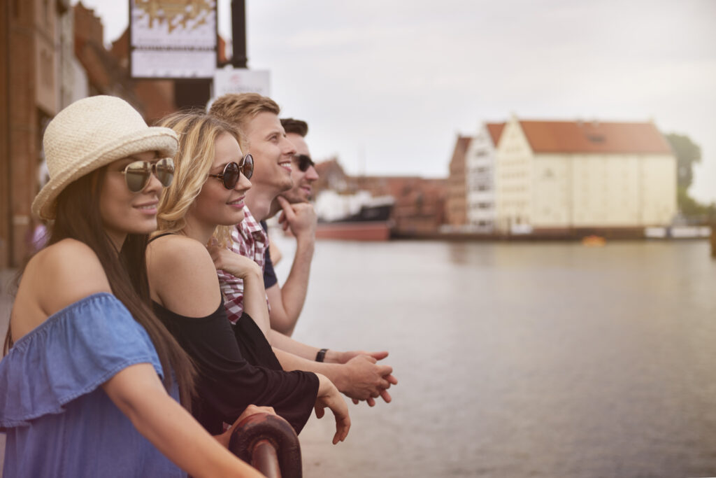 A group of 4 friends stand on the banks of a canal, smiling at the view and enjoying their time together.