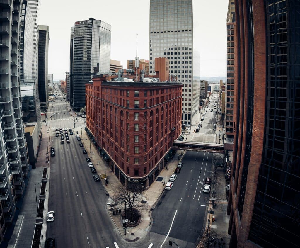 Photo taken at the intersection of two streets in the Central district of Denver, Colorado, USA. The building at the intersection is made of red brick, in an industrial style. The rest of the photo is fairly monochrome, in shades of grey, black and white.