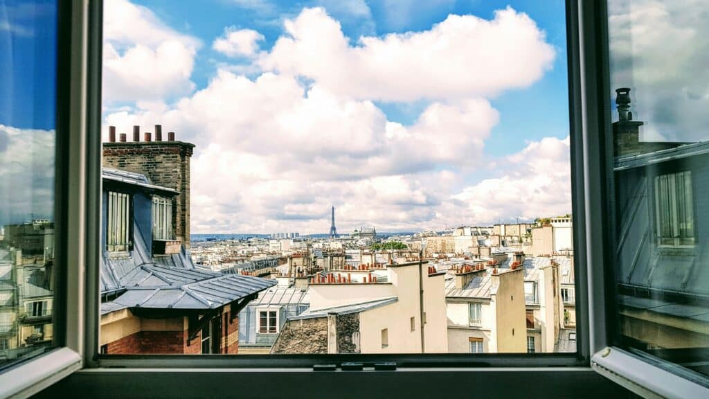 The view is taken from a window overlooking the rooftops of Paris, showing the Eiffel Tower in the background.