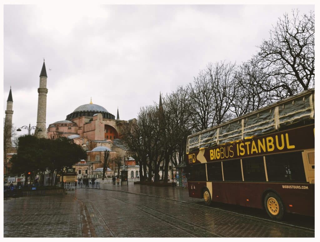 A large tourist bus wends its way through the streets of Istanbul, passing a famous monument.