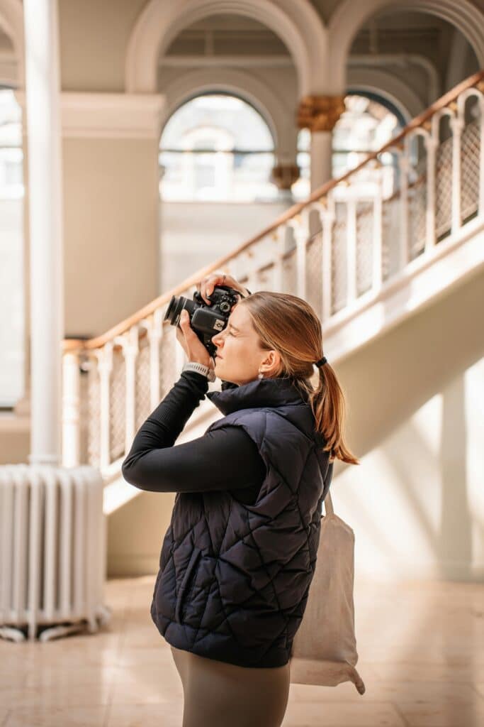 A blonde woman taking an indoor photo in a building with an elegant, uncluttered style.