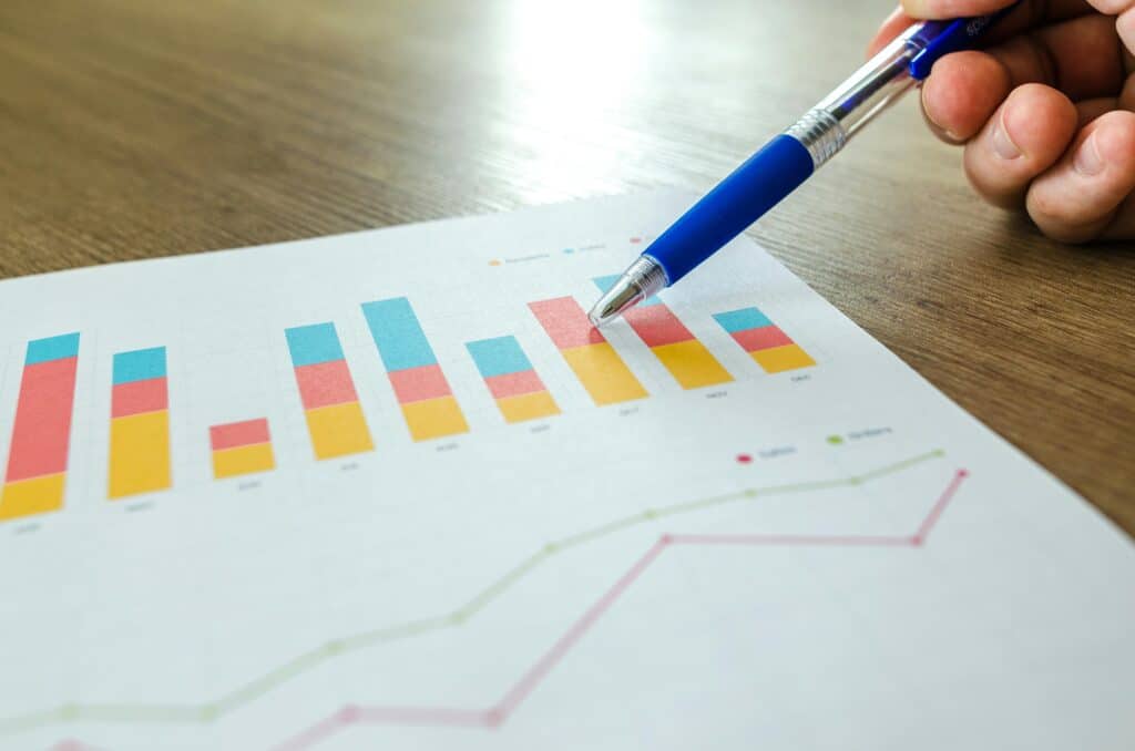 One hand holds a pen and points a bar graph at a sheet of paper on a table. Below the bar graph is a curve showing the evolution of two factors.