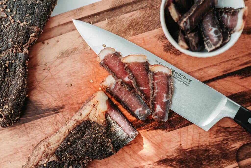 Culinary photo of slices of dried meat just cut on a wooden chopping board. Some of the slices are in a bowl on the board.