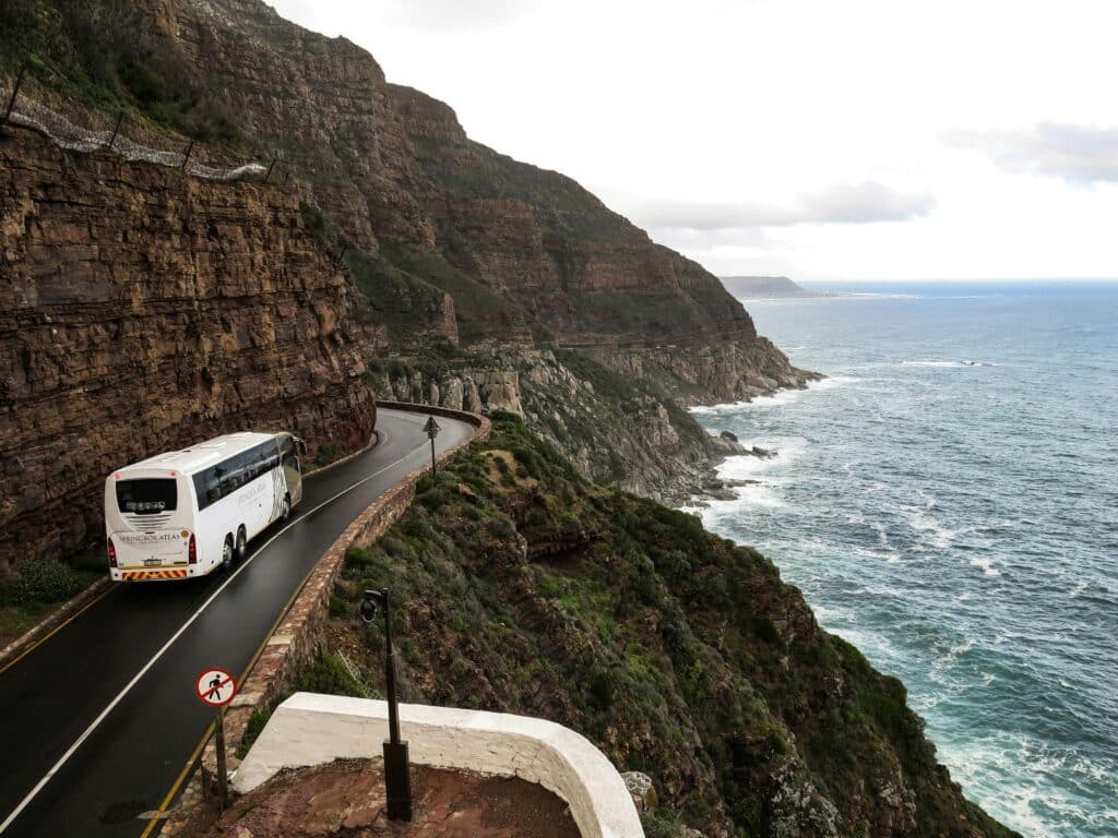 A bus drives along a coastal road in Bo-Karoo, South Africa. The road between the cliffs and the ocean is winding and narrow.