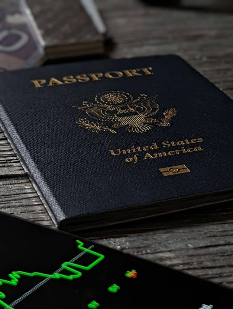 The photo shows an American passport on a table, next to a mobile phone showing the stock market price, and a luxury brand wallet.