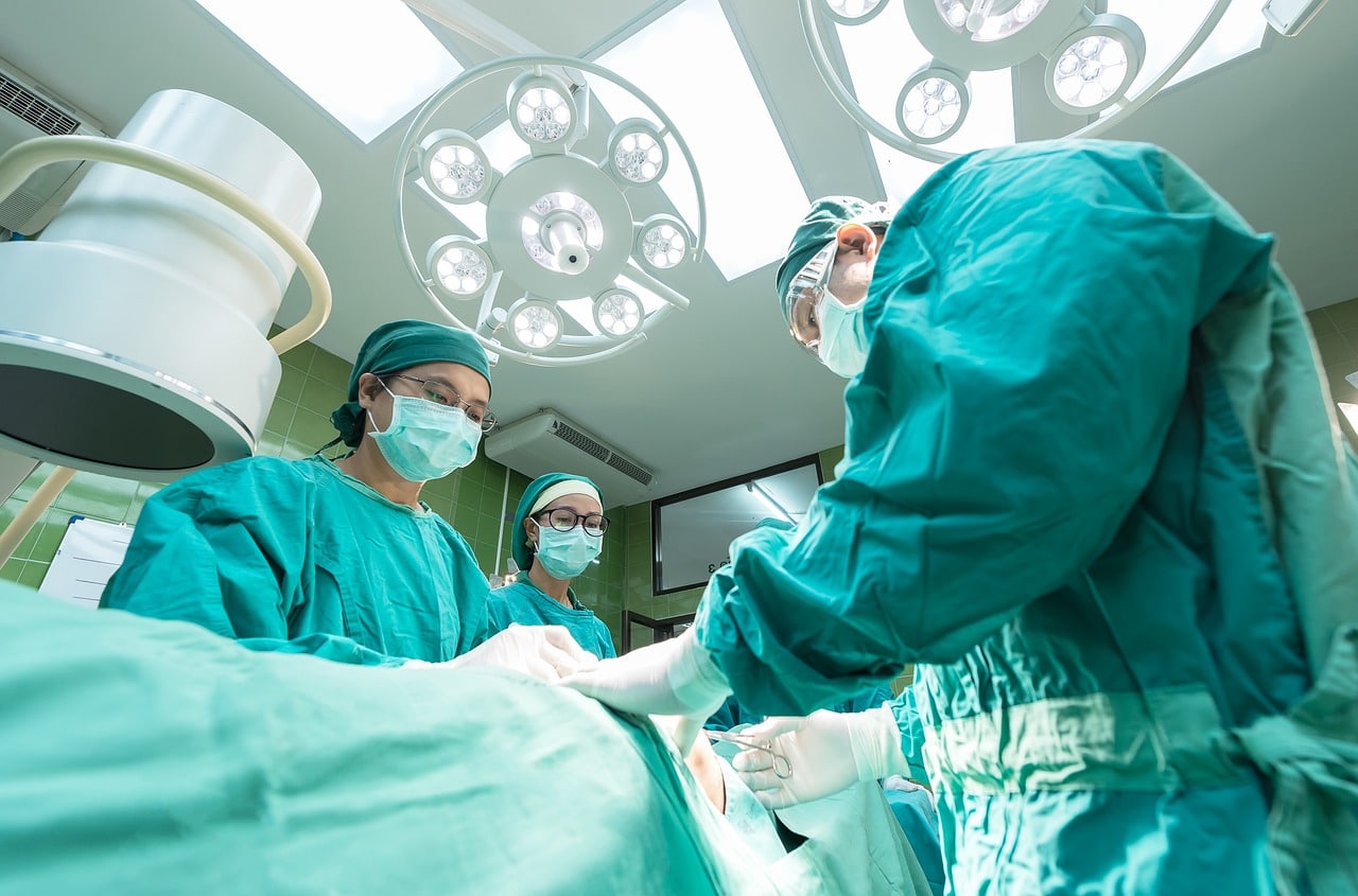 The photo shows a surgical team of three performing an operation on a patient in a hospital.