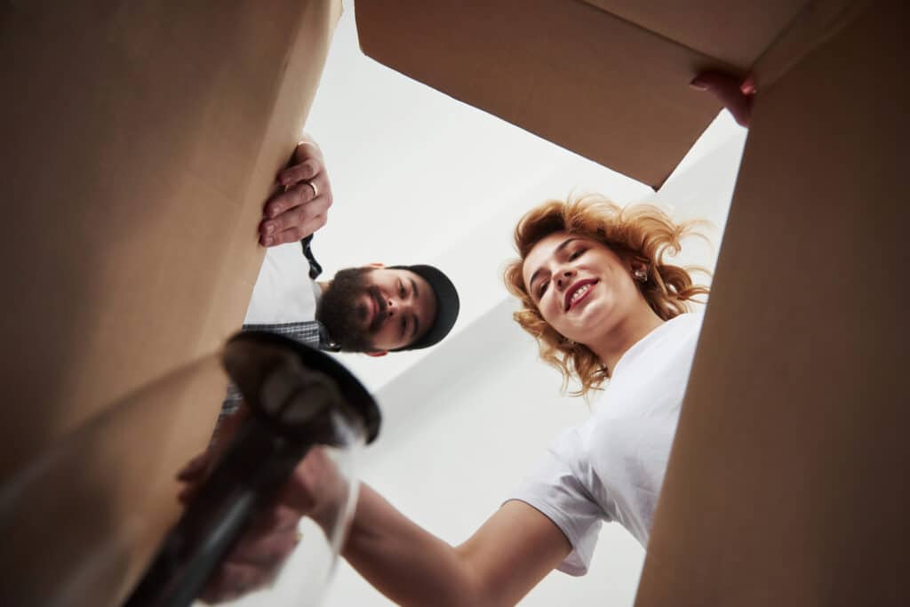 The photo is taken from the inside of a cardboard box and shows a couple opening the box as they move house.