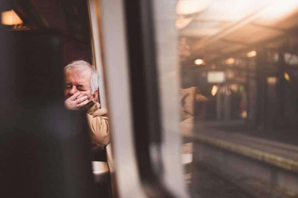 An old man is fast asleep, leaning against the train window sill.