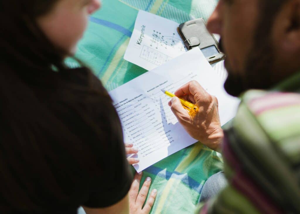 A teacher gives a language lesson to his pupil, and uses a pen to underline phrases to be completed on an exercise sheet, explaining what needs to be filled in.