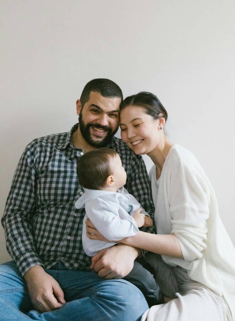 Family photo of two parents and their young son of Middle Eastern origin, taken against a white background. The parents are smiling and the baby is looking at his mother.