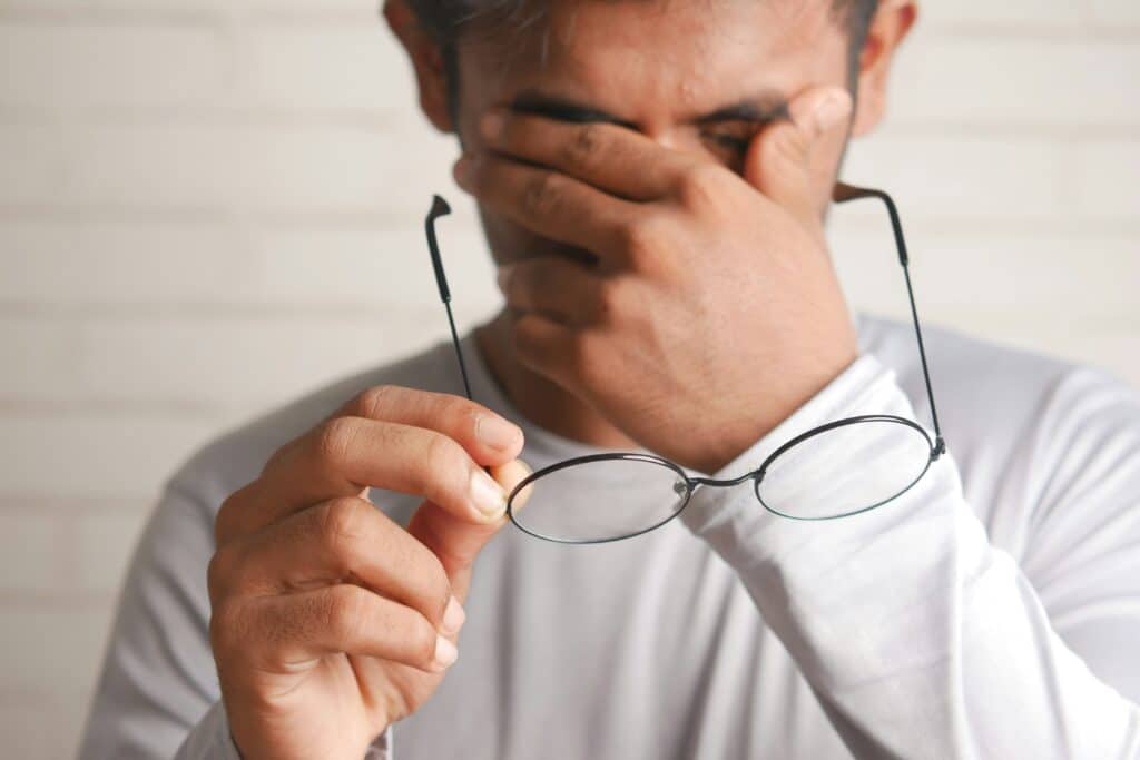 A man holds his face with one hand and his glasses with the other and feels a sensation of pain or discomfort.